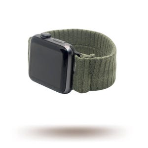 May include: A black smartwatch with a dark green ribbed knit strap. The watch face is black and rectangular. The strap is made of a soft, textured material. The watch is shown against a white background.