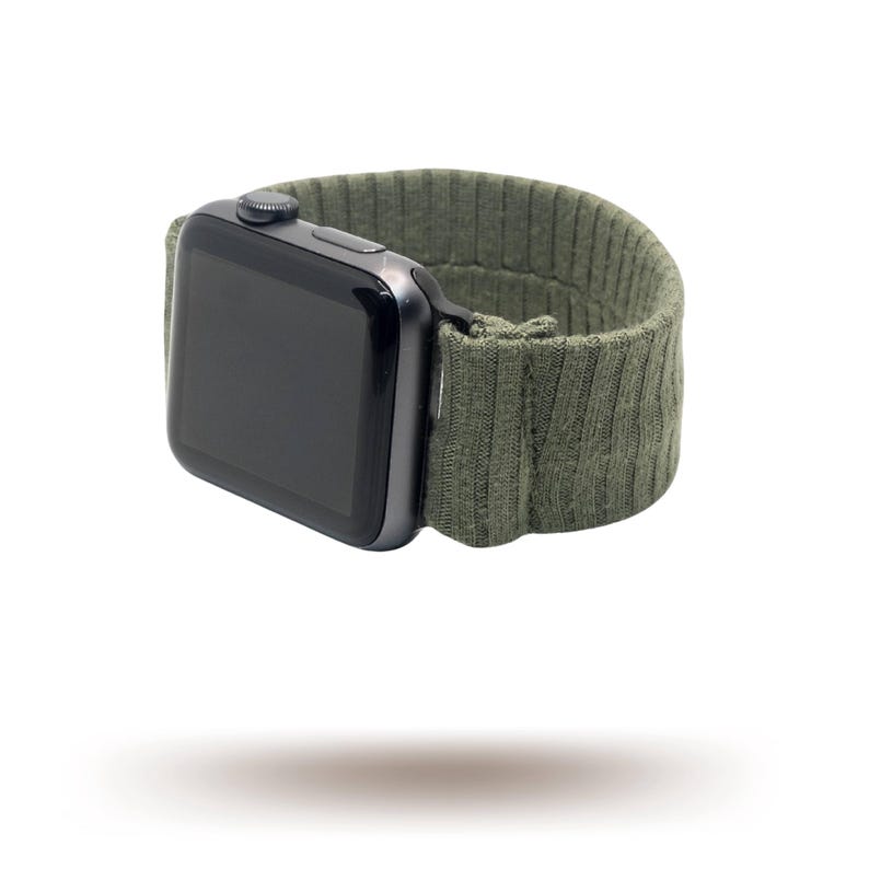 May include: A black smartwatch with a dark green ribbed knit strap. The watch face is black and rectangular. The strap is made of a soft, textured material. The watch is shown against a white background.