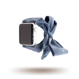 Könnte beinhalten: Ein blaues Stoffarmband mit einem weißen Apple Watch-Zifferblatt. Das Armband ist zu einer Schleife gebunden.