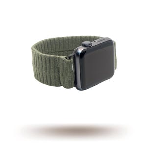 May include: An olive green ribbed knit Apple Watch strap with a black smartwatch. The strap is made of a soft, textured material and wraps around the watch face. The watch has a dark screen and a silver crown.
