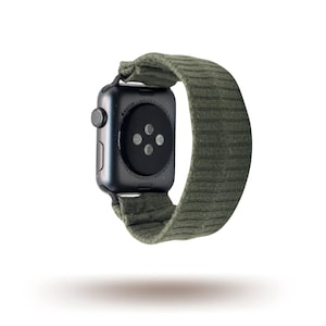 May include: A black smartwatch with a green ribbed fabric strap. The watch face is black with a circular button. The strap is a muted green colour and appears to be made of a soft, textured material.