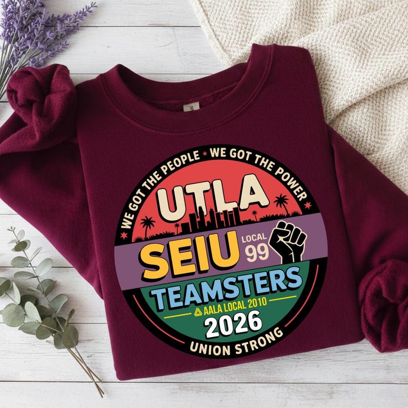 May include: Burgundy sweatshirt with a circular graphic featuring the text "UTLA SEIU TEAMSTERS Local 99" and "We Got The People, We Got The Power". The graphic includes a cityscape silhouette, palm trees, and a raised fist. The text "2026 Union Strong" is also present.