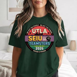 May include: Dark green t-shirt with a circular graphic featuring the text "UTLA SEIU Teamsters Local 99" and the phrases "We Got The People, We Got The Power" in red. The graphic also includes a fist and the year 2026.
