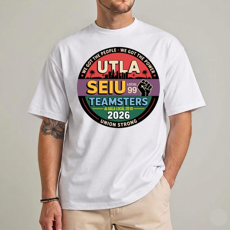 May include: White t-shirt with a circular graphic featuring the text "UTLA SEIU Teamsters 2026 Union Strong." The design includes a cityscape silhouette, a raised fist, and the phrases "We Got The People" and "We Got The Power."