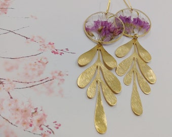 May include: Gold earrings with a delicate leaf design and a round pendant featuring pressed purple flowers.