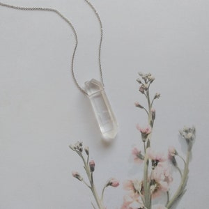 May include: A silver chain necklace with a clear quartz crystal pendant. The pendant is a long, thin, pointed crystal.