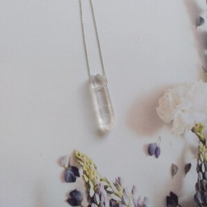 May include: A silver chain necklace with a clear quartz crystal pendant. The crystal is faceted and has a pointed tip.