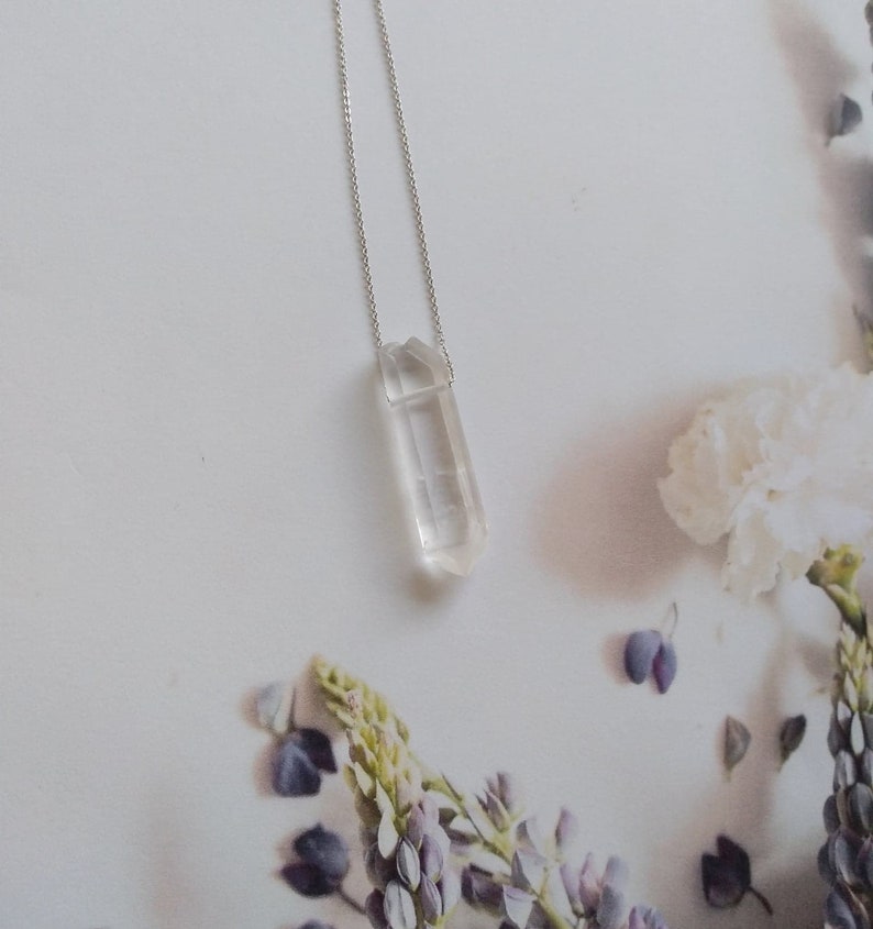 May include: A silver chain necklace with a clear quartz crystal pendant. The crystal is faceted and has a pointed tip.