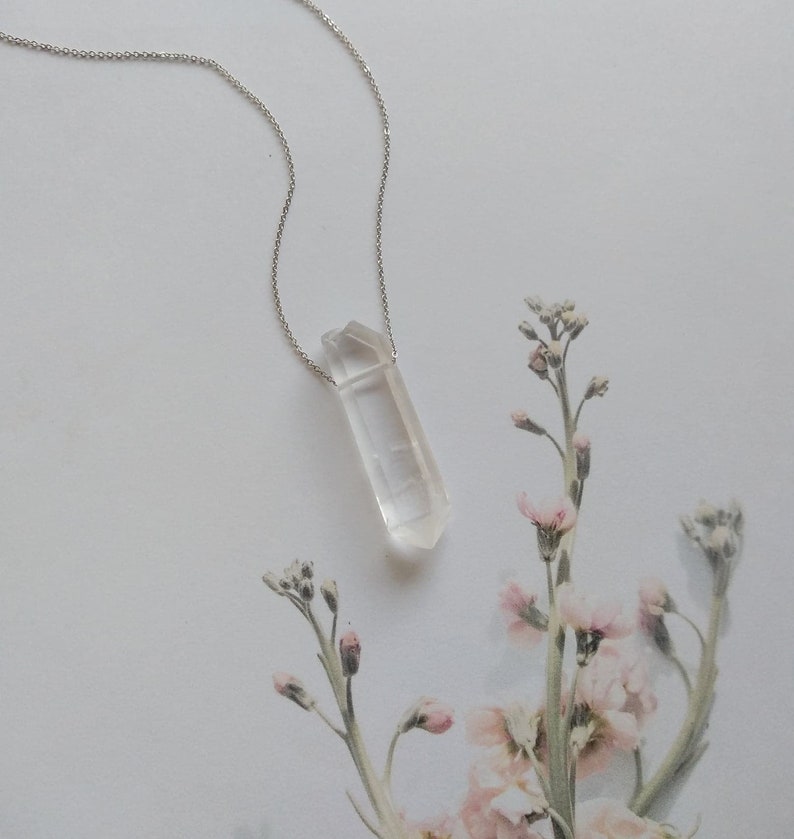 May include: A silver chain necklace with a clear quartz crystal pendant. The pendant is a long, thin, pointed crystal.