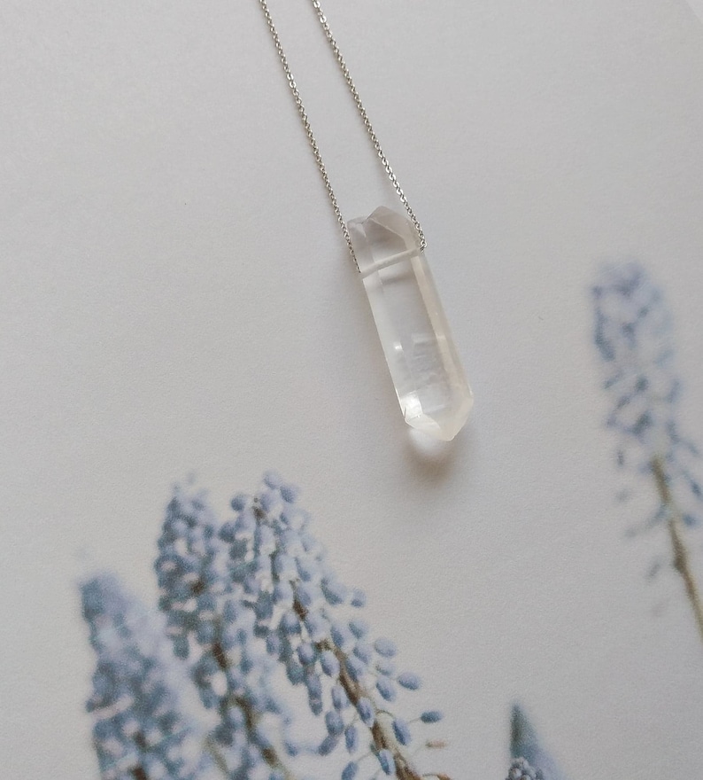 May include: A clear quartz crystal pendant on a silver chain. The pendant is a long, thin, pointed shape.