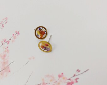 May include: A pair of gold-toned stud earrings with a round, clear resin design featuring pressed dried flowers in shades of orange, yellow, red, and purple.