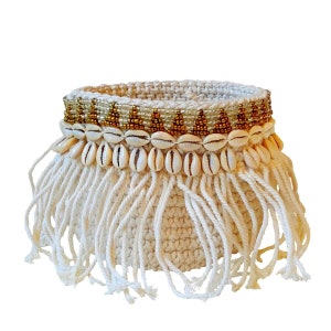 Peut inclure: Un panier en crochet blanc avec une bordure en franges. Le panier est décoré d'une bande de perles dorées et d'une rangée de coquillages blancs.