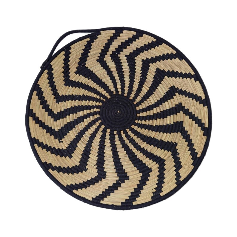 May include: Circular woven basket featuring a black and natural zig-zag design. The basket has a black central area and a black handle. It is made from natural fibres.