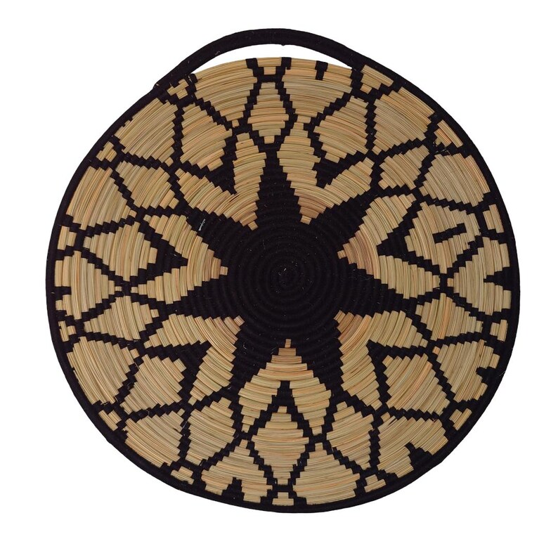 May include: Circular woven basket featuring a black and natural geometric starburst pattern. The basket has a black handle and rim. The natural colour is a light tan. The basket is made of woven natural fibres.