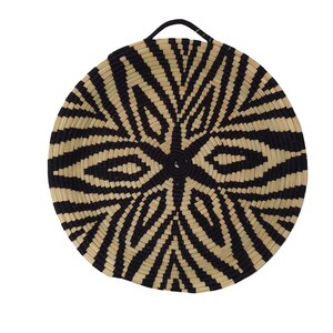May include: Circular woven basket with a black and natural geometric design. It features a handle for hanging. The pattern has a central starburst with radiating lines. This decorative item is suitable for wall decor and measures approximately 40cm in diameter.