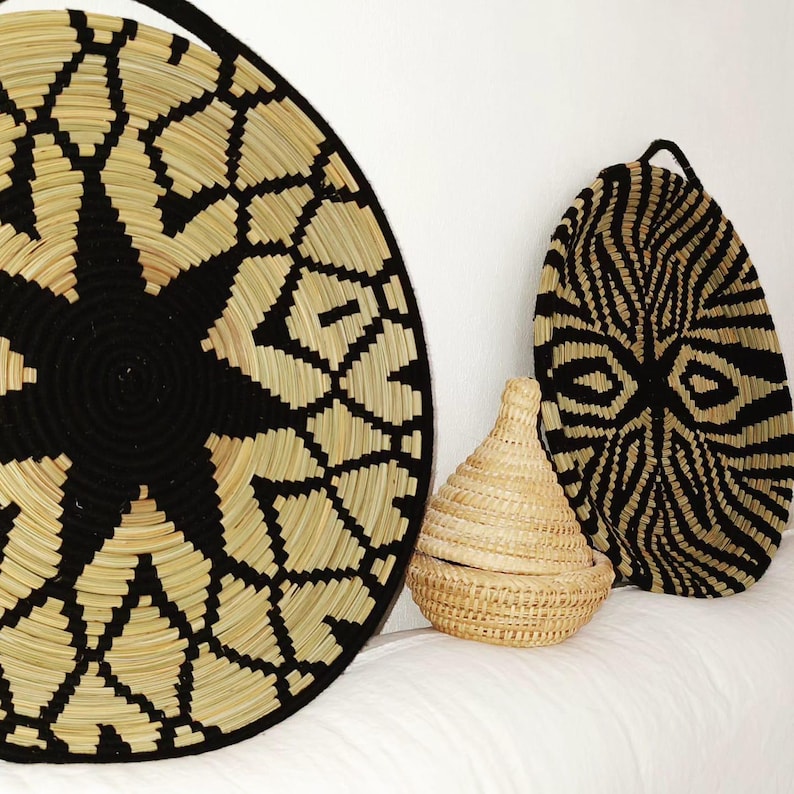 May include: A selection of woven baskets featuring black and natural fibre designs. The large, round basket on the left has a geometric pattern. The oval basket on the right has a zebra-like pattern. A small, lidded basket is in front.
