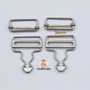 May include: Two silver metal garment clasps, one with a hook and one without. The clasp with the hook is 38mm wide.