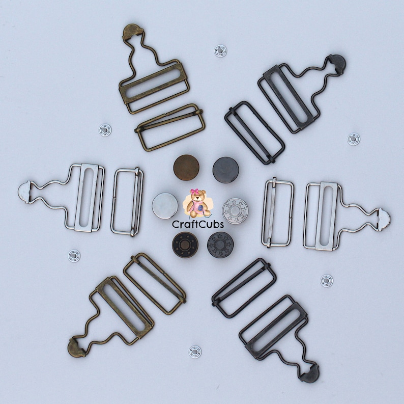 May include: Six metal clasps, two in antique brass, two in silver, and two in black. The clasps are designed for attaching clothing or other fabric items. The clasps are arranged in a star shape on a white background.