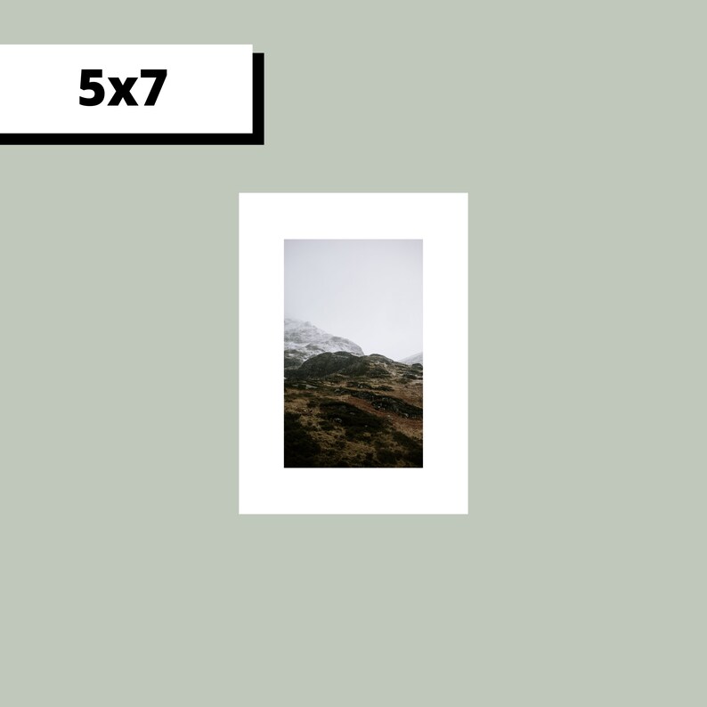 May include: A photograph of a mountain range with a snowy peak in the distance. The mountain is covered in green vegetation and the sky is cloudy.