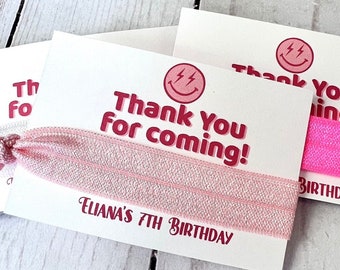 Könnte beinhalten: Rosa-weiße Dankeschön-Geschenkbox mit einem rosa elastischen Haargummi. Die Karte zeigt ein Smiley-Gesicht mit Blitzen und den Text "Danke, dass du gekommen bist!" und "Eliana's 7th Birthday".