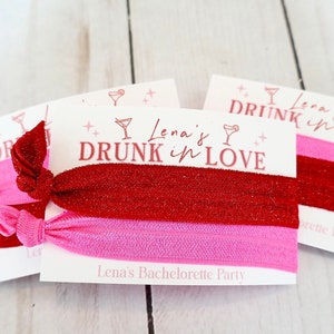May include: Two sets of red and pink hair ties with glitter on a white card that says "Lena's Drunk in Love" and "Lena's Bachelorette Party".