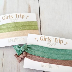 May include: Two sets of hair ties with cards. Each set has two hair ties, one green and one beige. The cards have the text "Girls Trip 2024" and "Nashville, TN".