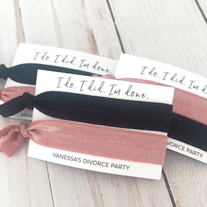 May include: Two sets of hair ties with a pink and black color scheme. The hair ties have a card attached to them that says "I do. I did. I'm done." and "Vanessa's Divorce Party".