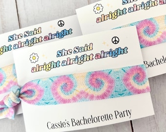 Może przedstawiać: Dwa gumki do włosów w stylu tie-dye z białą kartką, na której napisano "She Said alright alright alright" i "Cassie's Bachelorette Party".