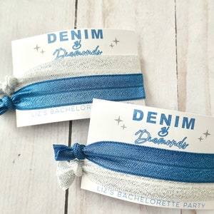 Peut inclure: Deux &eacute;lastiques &agrave; cheveux bleus et argent&eacute;s avec une carte blanche qui dit "Denim & Diamonds" et "Liz's Bachelorette Party".