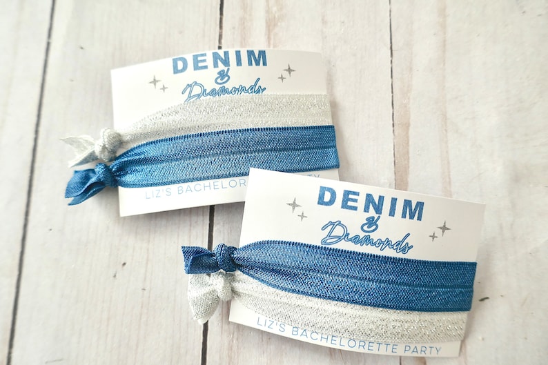 Peut inclure: Deux &eacute;lastiques &agrave; cheveux bleus et argent&eacute;s avec une carte blanche qui dit "Denim & Diamonds" et "Liz's Bachelorette Party".