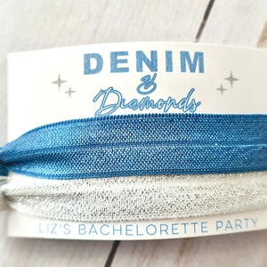 Peut inclure: Un &eacute;lastique &agrave; cheveux bleu et argent&eacute; avec une carte blanche sur laquelle est inscrit "Denim & Diamonds" et "Liz's Bachelorette Party".