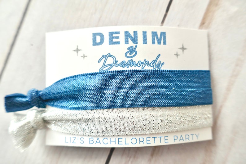 Peut inclure: Un &eacute;lastique &agrave; cheveux bleu et argent&eacute; avec une carte blanche sur laquelle est inscrit "Denim & Diamonds" et "Liz's Bachelorette Party".