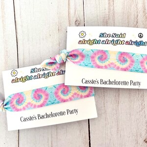 May include: Two tie-dye fabric wristbands with a white card attached to each. The card says "She Said alright alright alright" and "Cassie's Bachelorette Party".