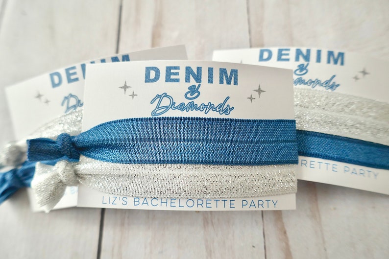 Peut inclure: Des &eacute;lastiques &agrave; cheveux bleus et argent&eacute;s avec une carte blanche sur laquelle est inscrit "Denim & Diamonds" et "Liz's Bachelorette Party".
