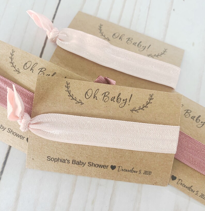 K&ouml;nnte beinhalten: Ein Set aus drei braunen Karten-Geschenken mit rosafarbenen Gummib&auml;ndern f&uuml;r Haare. Die Karten haben den Text "Oh Baby!" und ein florales Design. Die Karten enthalten auch den Text "Sophia's Baby Shower" und das Datum "December 5, 2020".