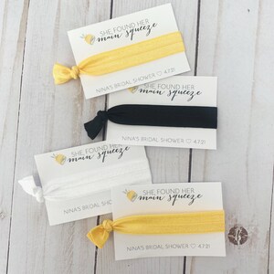 May include: Four cards with lemon illustrations and the text "She found her main squeeze" with a yellow, black, white, and yellow hair tie on each card. The cards also include the text "Nina's Bridal Shower 4.7.21".
