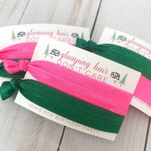 May include: Two pink and green hair ties with a white card that says "glamping hair don't care" and "Mia's 8th birthday party".