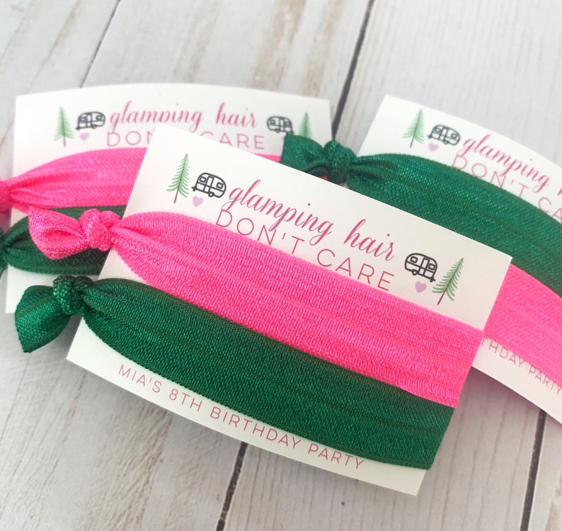 May include: Two pink and green hair ties with a white card that says "glamping hair don't care" and "Mia's 8th birthday party".