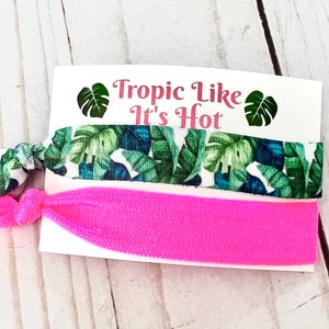 Op de afbeelding: Twee haar elastiekjes, een met een tropische bladerenprint en de andere effen roze. De kaart staat "Tropic Like It's Hot".