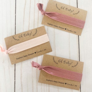 K&ouml;nnte beinhalten: Drei braune Karten-Geschenke mit rosafarbenen Gummib&auml;ndern f&uuml;r Haare. Jede Karte tr&auml;gt den Text "Oh Baby!" und "Sophia's Baby Shower December 5, 2020".