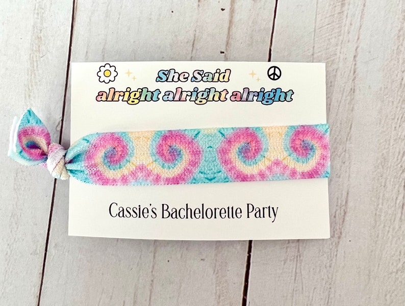 May include: A white card with the text "She Said alright alright alright" and a tie-dye elastic hair tie. The card also says "Cassie's Bachelorette Party".