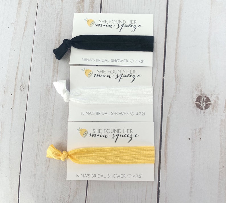 May include: Three hair ties with cards that say "She found her main squeeze" and "Nina's Bridal Shower 4.7.21". The hair ties are black, white, and yellow.