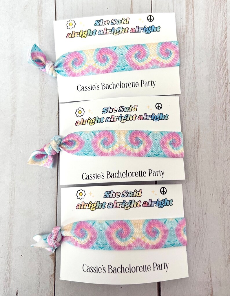 May include: Three tie-dye fabric hair scrunchies with the text "She Said alright alright alright" and "Cassie's Bachelorette Party" printed on white cards.