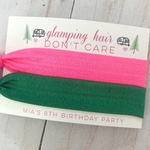 May include: Two hair ties, one pink and one green, with a card that says "glamping hair don't care" and "Mia's 8th birthday party".