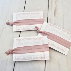 K&ouml;nnte beinhalten: Drei wei&szlig;e Karten mit rosafarbenen Gummib&auml;ndern befestigt. Jede Karte hat einen dekorativen Rand und den Text "Cutie Linda" in Kursivschrift.