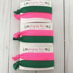 May include: Three sets of hair ties with pink and green elastic bands. Each set has a card attached with the text "glamping hair don't care" and "MIA'S 8TH BIRTHDAY PARTY".