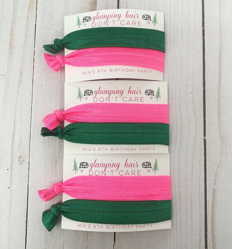 May include: Three sets of hair ties with pink and green elastic bands. Each set has a card attached with the text "glamping hair don't care" and "MIA'S 8TH BIRTHDAY PARTY".