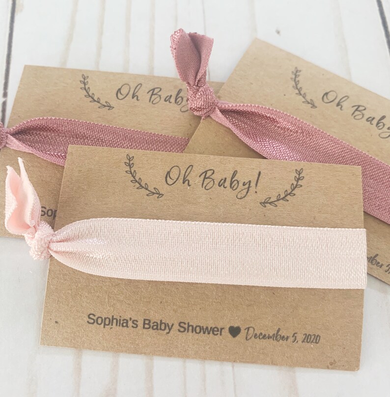 K&ouml;nnte beinhalten: Ein Set aus drei braunen Karten-Geschenken mit rosafarbenen Gummib&auml;ndern f&uuml;r Haare. Die Karten haben den Text "Oh Baby!" und "Sophia's Baby Shower December 5, 2020".