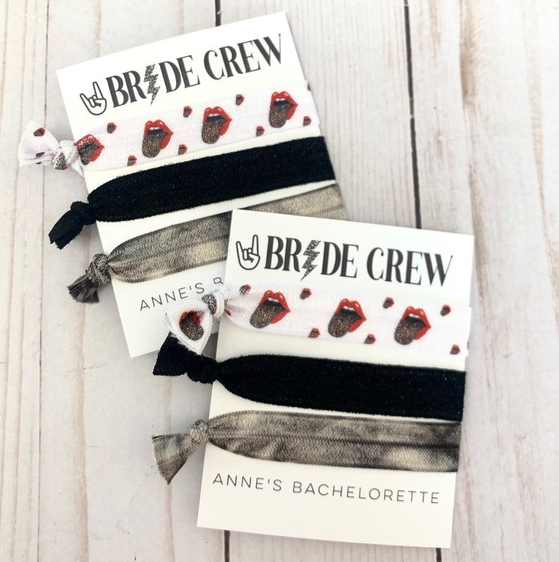 K&ouml;nnte beinhalten: Set aus drei Haargummis mit wei&szlig;em Hintergrund und einem Muster aus roten Lippen und einem Rock'n'Roll-Handsymbol. Die Haargummis sind mit einer Karte verpackt, auf der "Bride Crew" und "Anne's Bachelorette" steht.