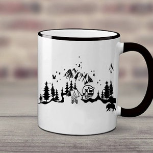 Puede incluir: Taza de cer&aacute;mica blanca con borde y asa negros. La taza presenta una ilustraci&oacute;n en blanco y negro de una escena de campamento con monta&ntilde;as, &aacute;rboles, una tienda de campa&ntilde;a, una caravana y una fogata. El texto "N" es visible en la esquina superior derecha de la taza.
